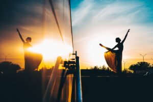 A ballet dancer dancing outside in the sunset with a reflection in a glass window